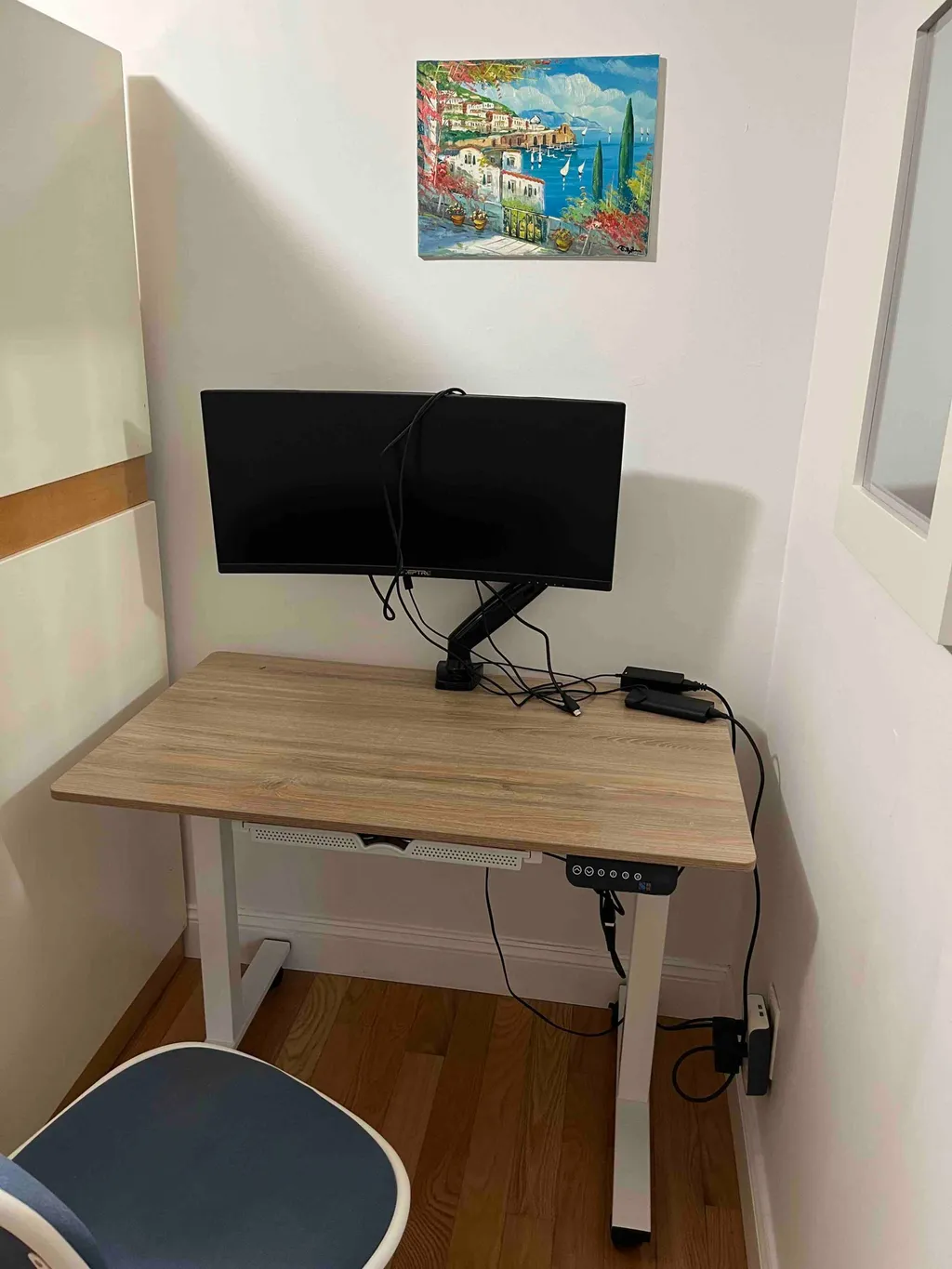 Desk with a monitor, cables, and a painting on the wall.
