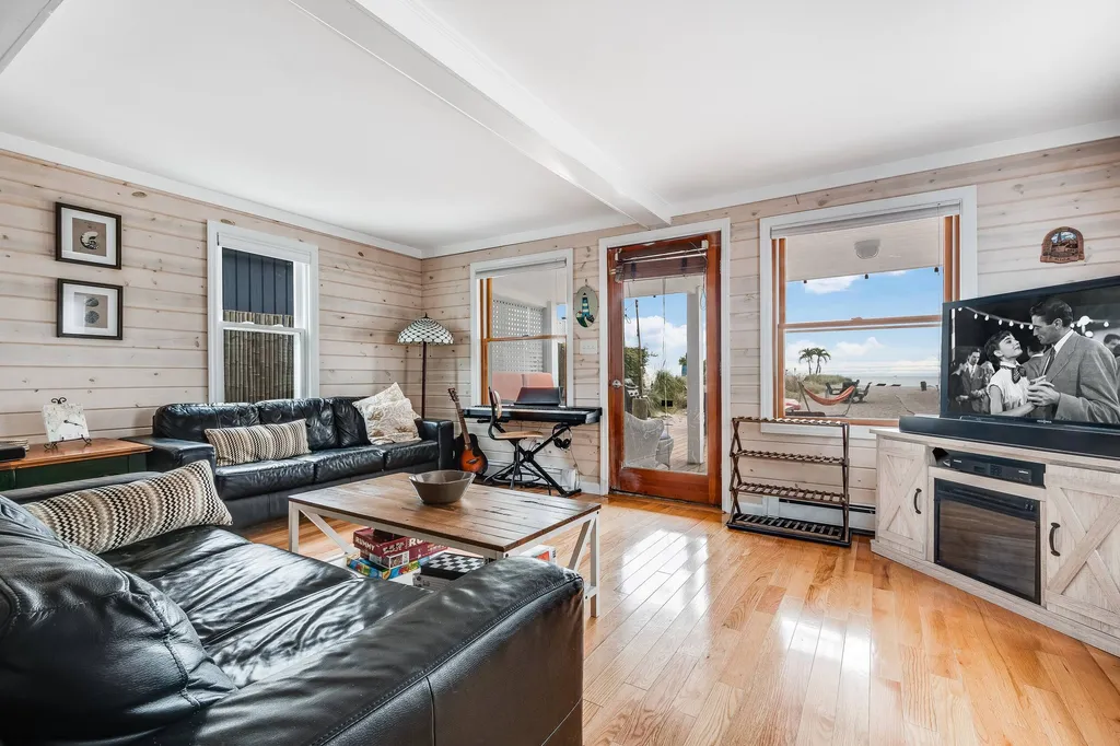 Living room with black leather sofas, a wooden coffee table, TV, keyboard and windows overlooking the beach.